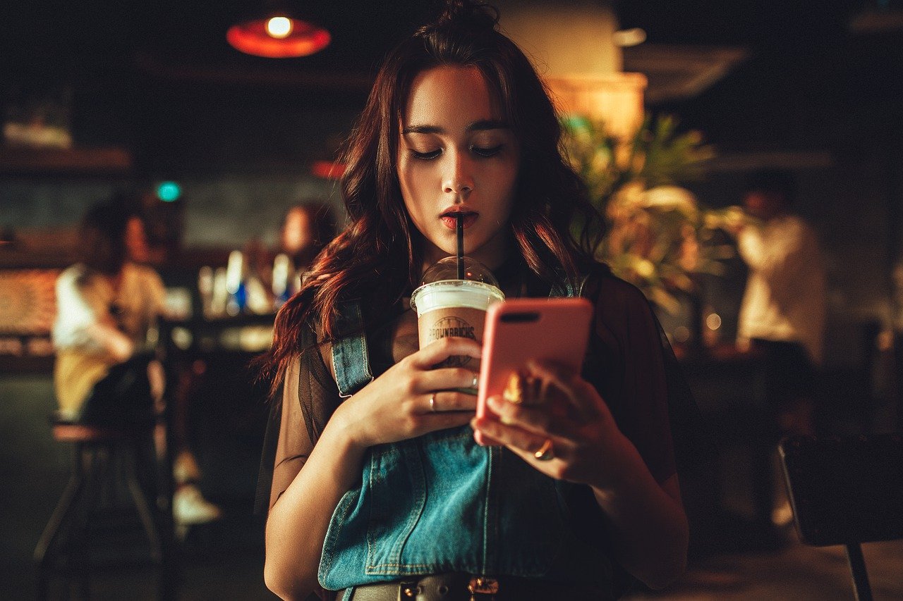 女性がドリンクを飲みながら携帯電話を眺めている画像
